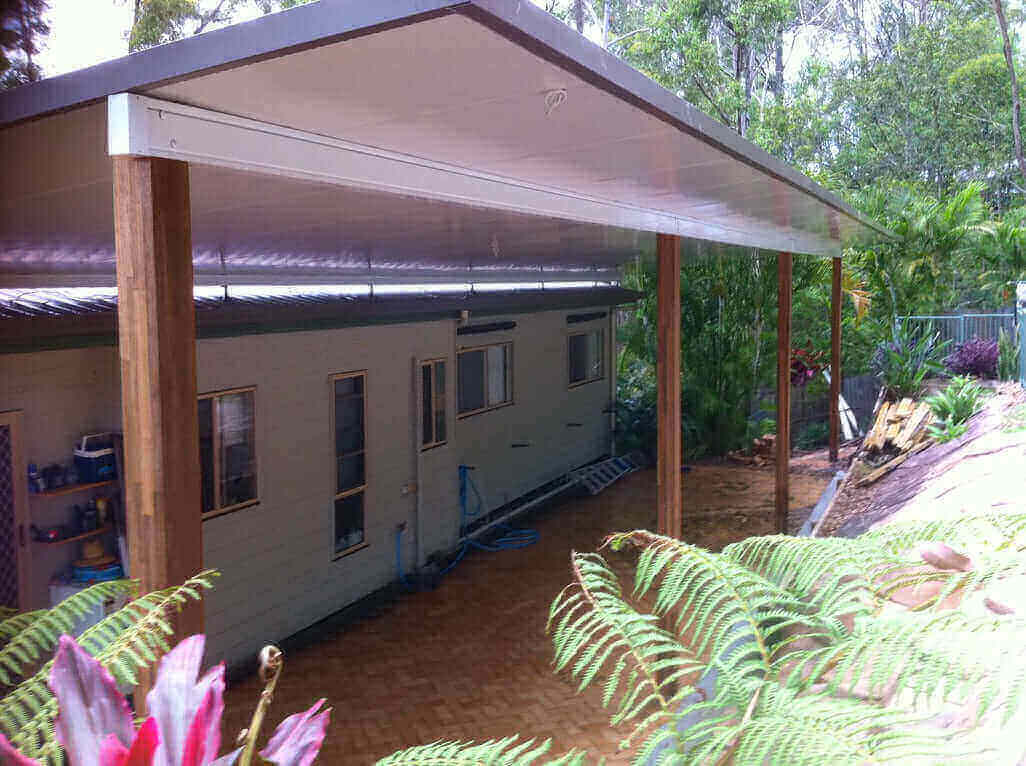 Contemporary insulated skillion patio carport with timber supports, offering poolside relaxation and scenic tree-lined surroundings.