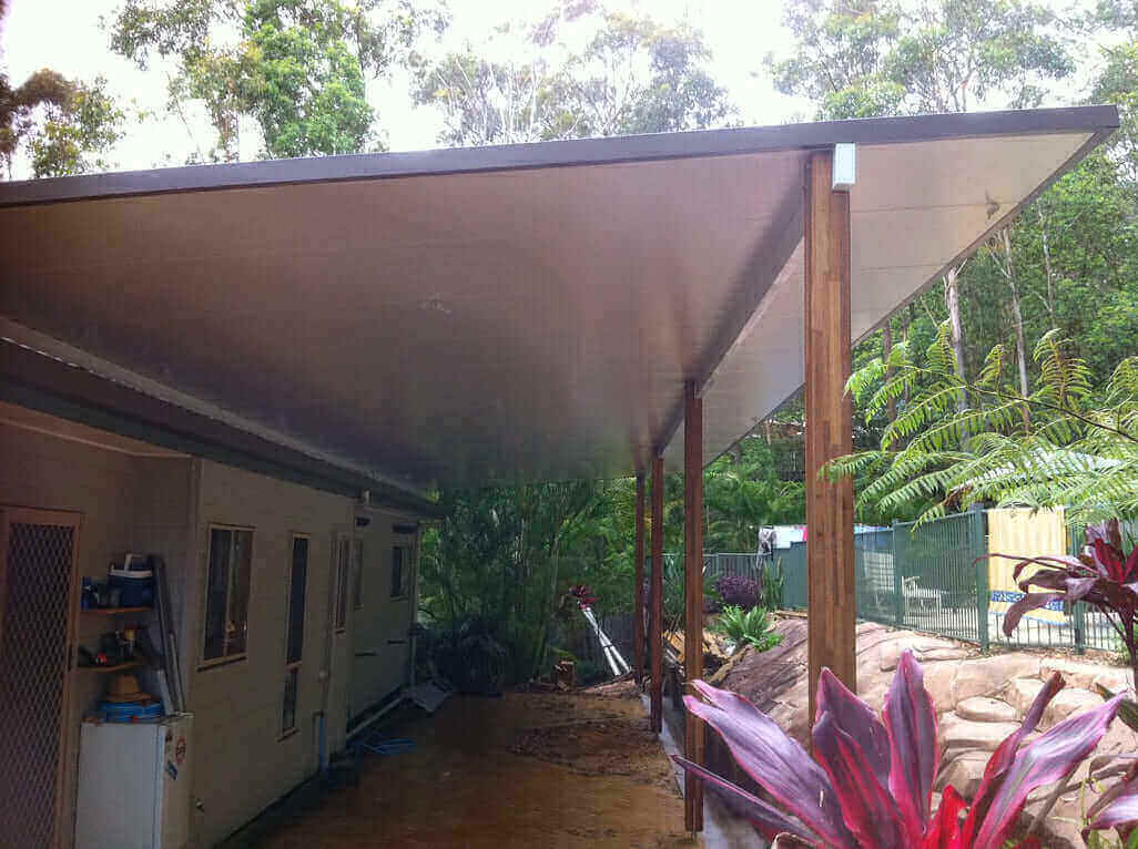Modern insulated skillion patio carport with stylish timber posts, set beside a pool and offering tranquil views of the surrounding trees.