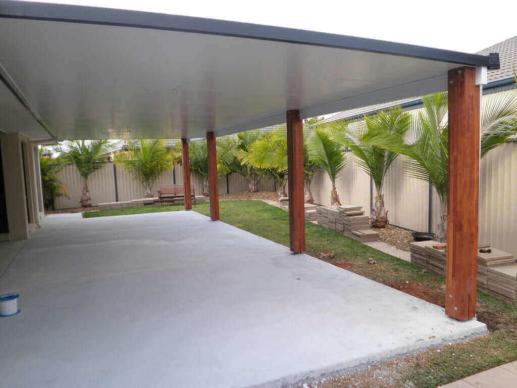 Attached insulated patio with wooden posts, concrete floor, and lush palm trees in a residential backyard.