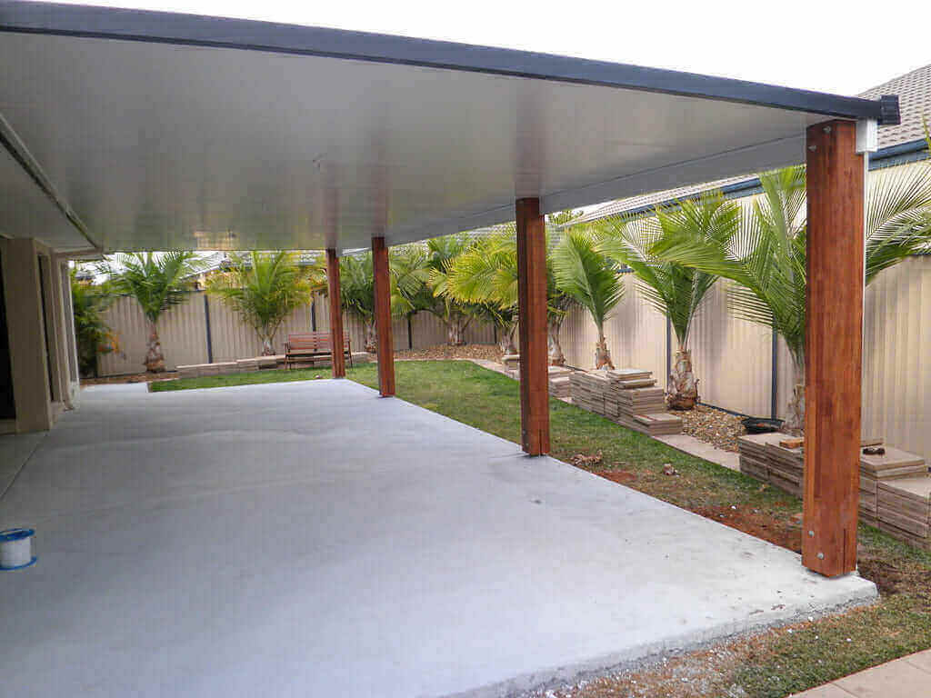 Sturdy insulated flyover patio roof with timber posts anchored by U plates, set atop a freshly laid concrete foundation.