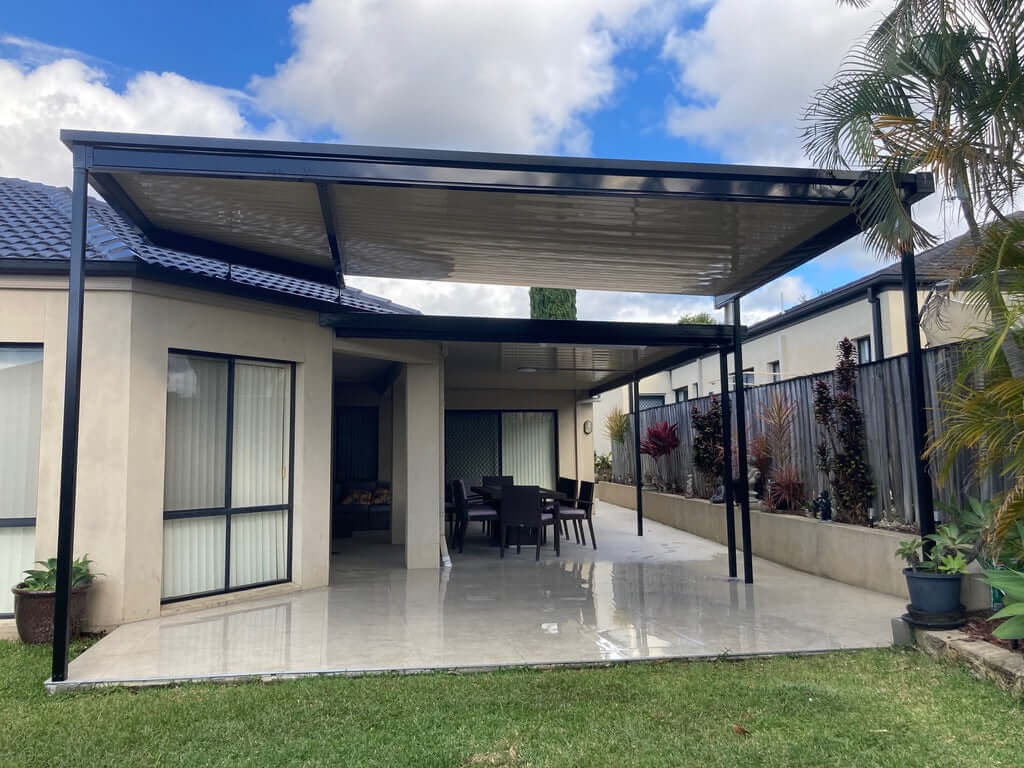 Insulated flyover patio roof with sleek black frame, creating a spacious covered outdoor entertaining area with tiled flooring and garden views.