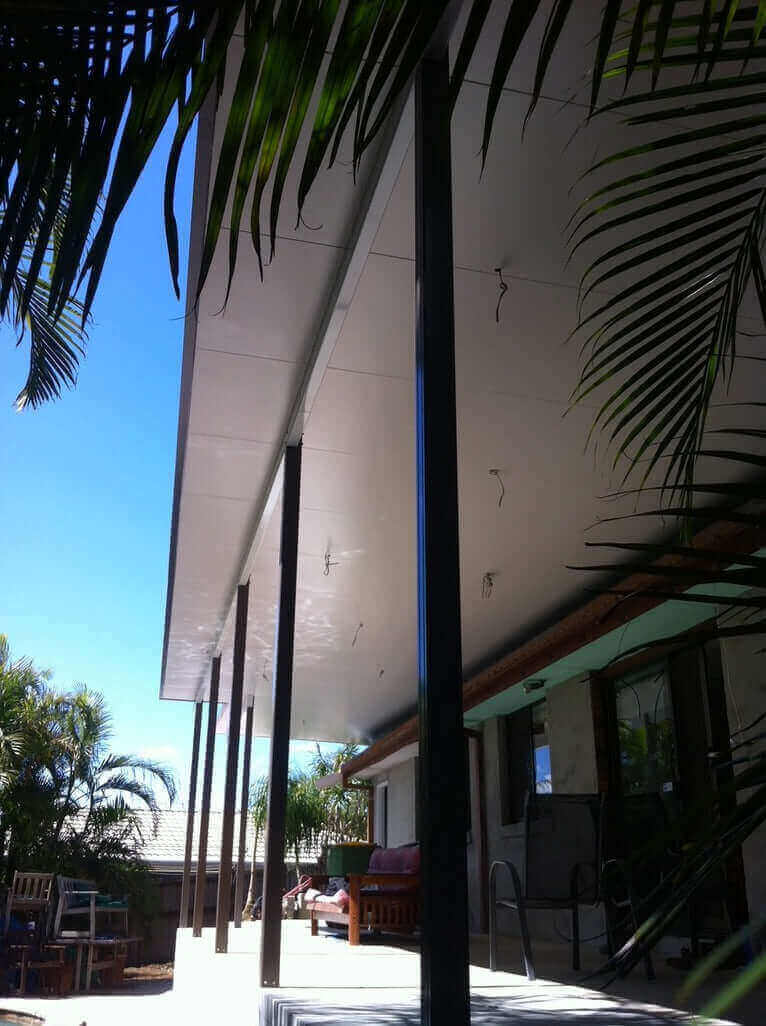 Attached patio roof creating a shaded outdoor area, viewed through tropical palm leaves beside a home