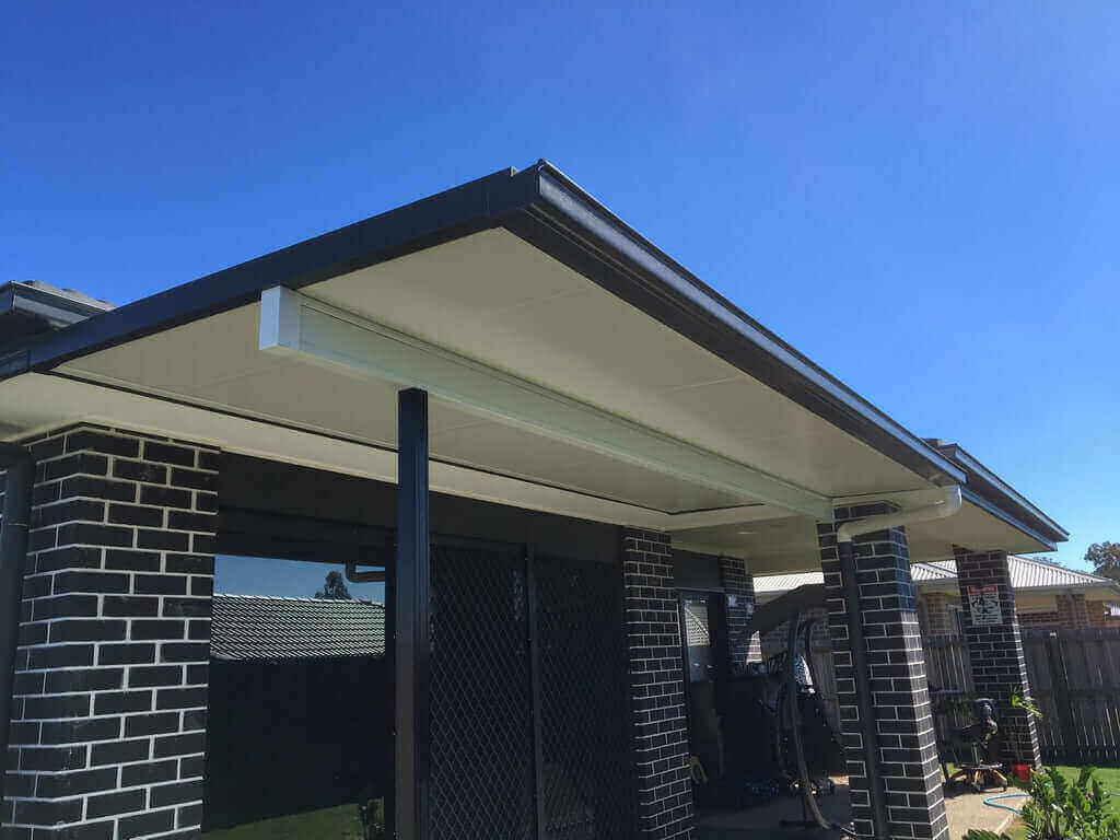 Insulated flat roof patio attached to brick home with steel posts and guttering, providing a modern covered outdoor living area for an Australian home.