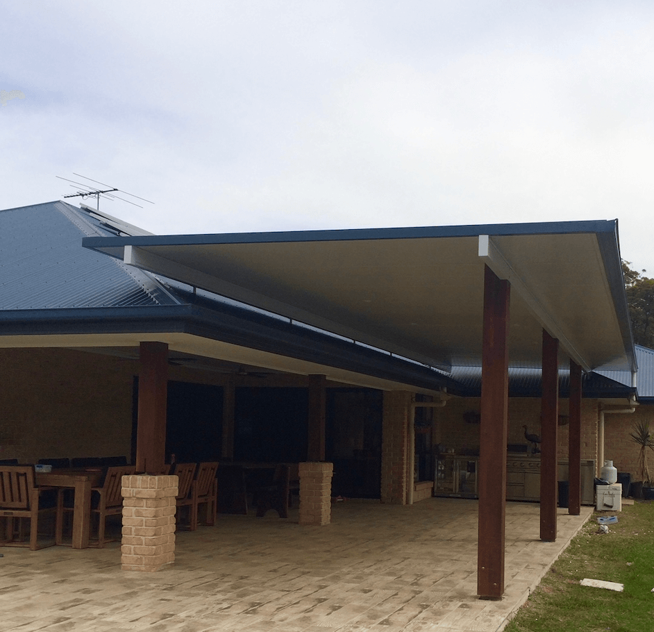 Modern insulated flyover patio roof attached to a brick home, featuring a sleek flat design with timber posts and a spacious outdoor entertaining area beneath.