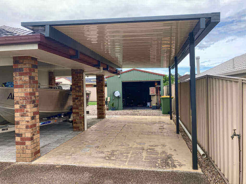 Single-skin patio carport with sleek modern roofing, extending alongside the home to provide sheltered vehicle parking and weather protection.