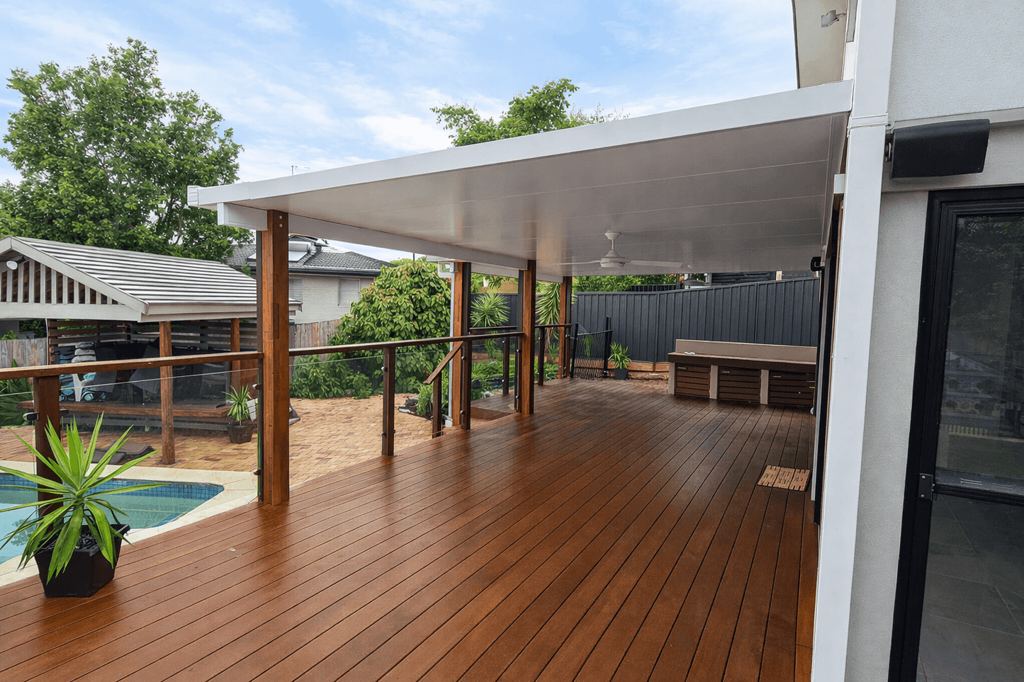 Modern insulated patio roof, fixed to wall, with sleek white ceiling panels supported by timber posts over a spacious wooden deck.