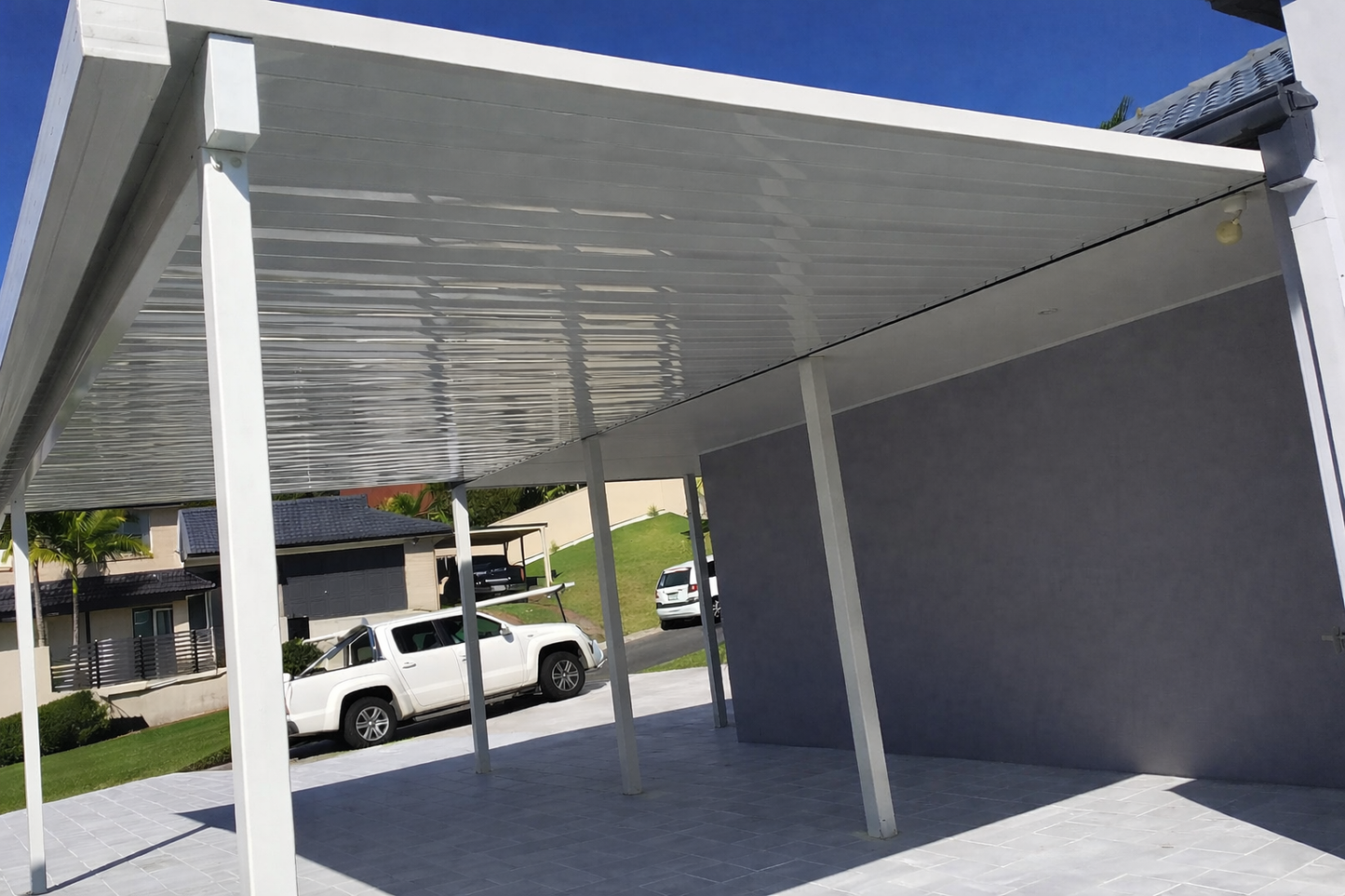 Contemporary white insulated panel carport attached to home with slim support posts and grey tiled driveway