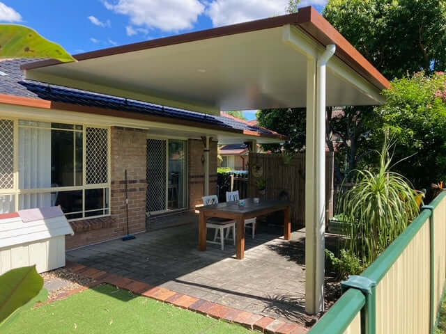 Single-skin flyover patio carport roof with posts fixed to the slab, featuring outdoor furniture, a dog house, and timber and aluminium fencing.