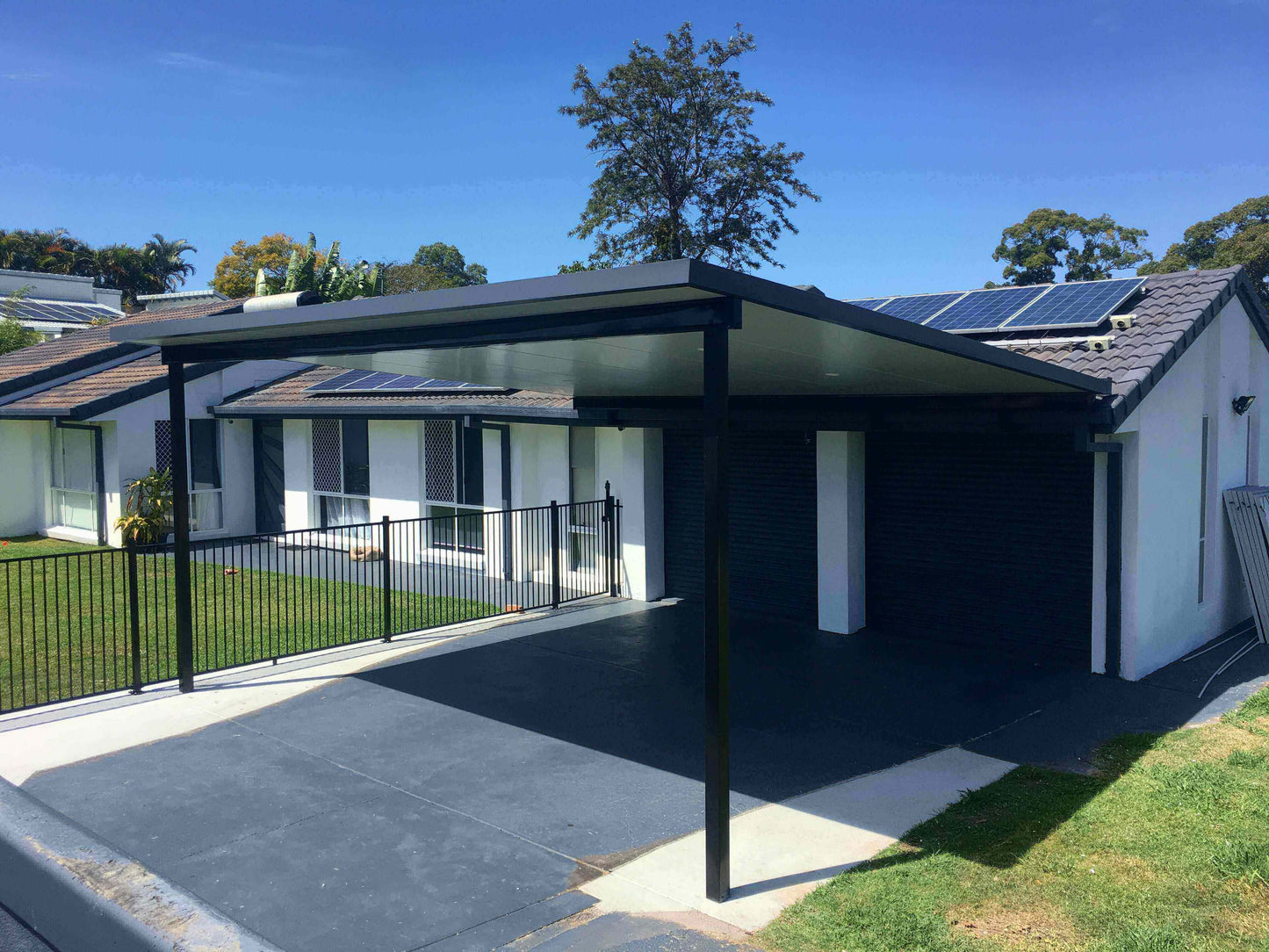 Reverse flyover patio colour-matched to the residence with striking ebony posts, surrounded by lawn and solar panels designed to provide heat protection.