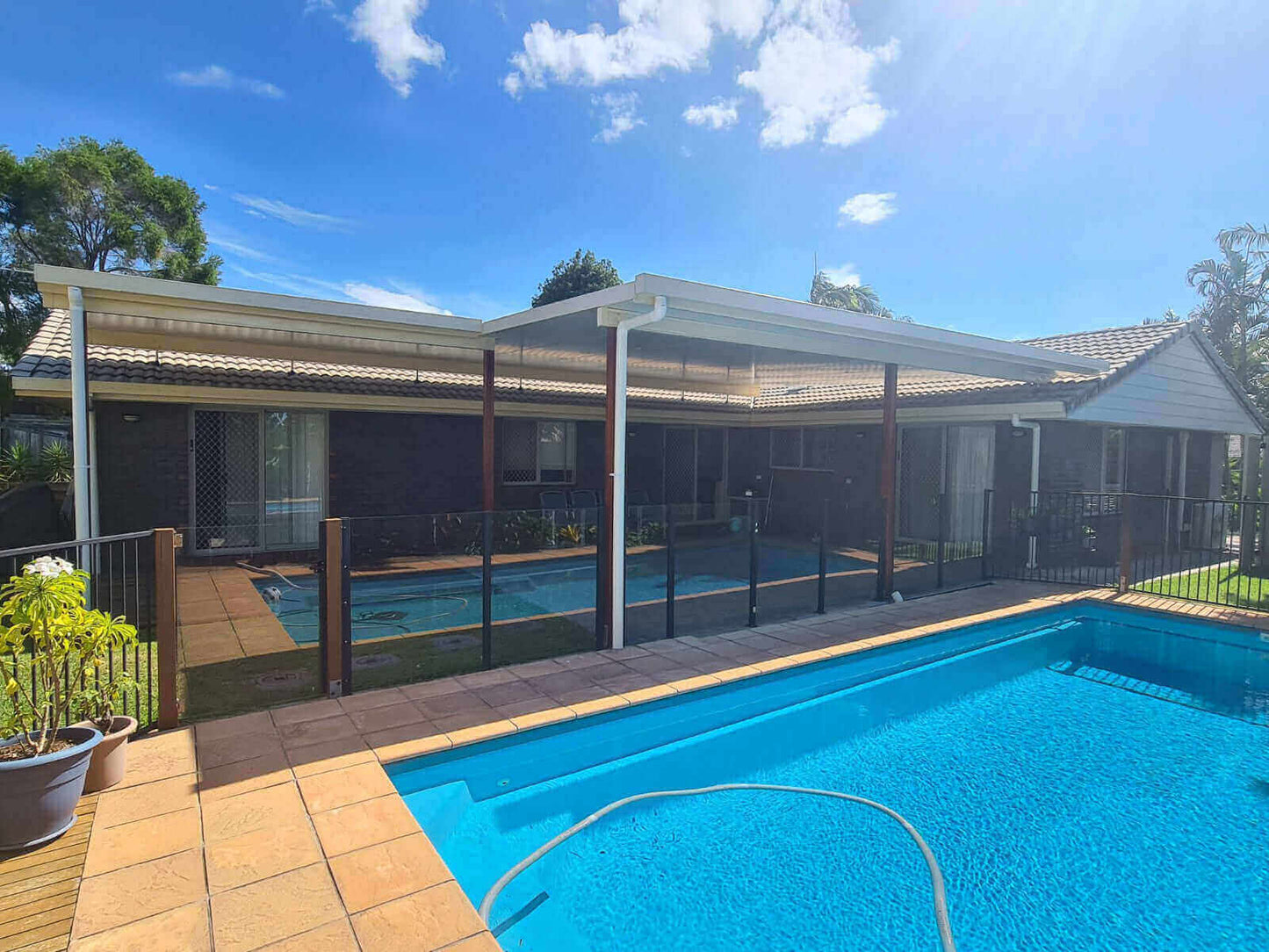 Flyover insulated patio featuring timber posts and glass fencing, seamlessly integrating with the pool and tiled space to create a backyard highlight that combines style and utility.