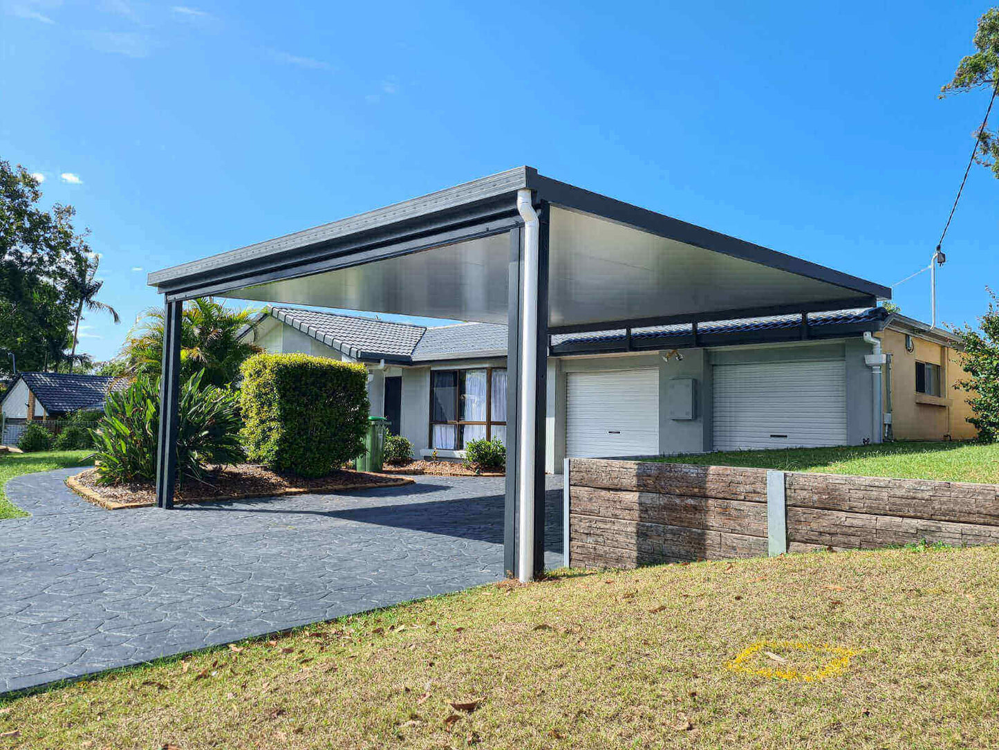 Stylish insulated flyover patio and carport, harmoniously connected to the home and retaining wall, providing easy double garage access and secure trailer storage.