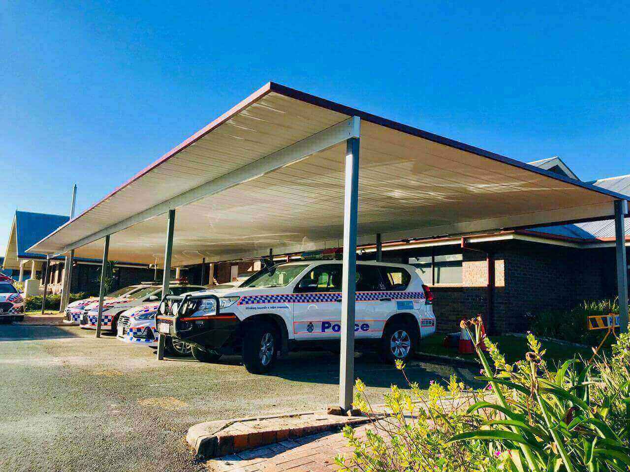 Free standing single skin patio/carport for commercial use offering all-weather coverage for police vehicles in a secure facility environment.