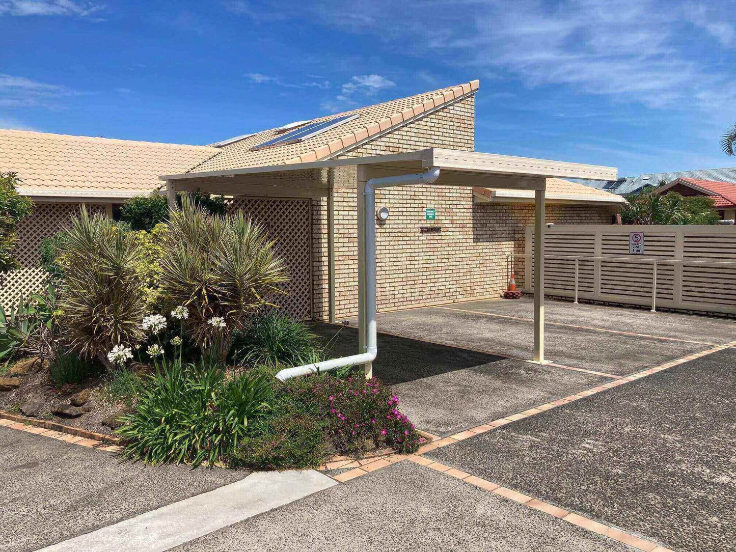 Free-standing patio/carport, standing independently in the driveway of a townhouse complex, with stunning blue sky views that enhance its sleek, modern design.