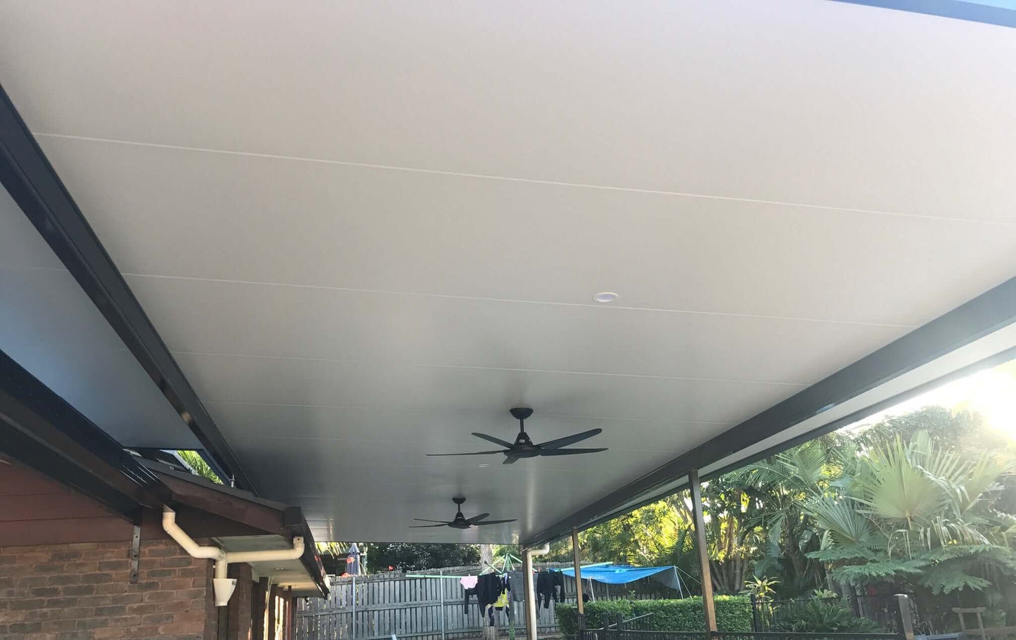 Long insulated patio roof with ceiling fans attached to a brick home, providing a cool, shaded outdoor living space.