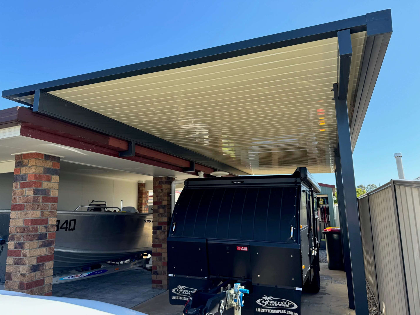 Modern insulated patio roof attached to a brick home, creating a dual-purpose covered space for vehicles, boats, or trailers.
