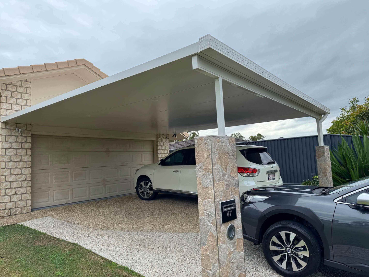 Double carport structure with flat insulated roofing, stone-clad posts, and space for two vehicles – enhancing home curb appeal and vehicle protection.