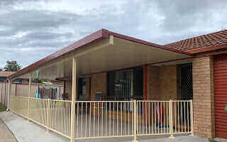 Attached single skin patio extension with a sloped roof and safety railing, creating a sheltered outdoor area alongside a brick home.