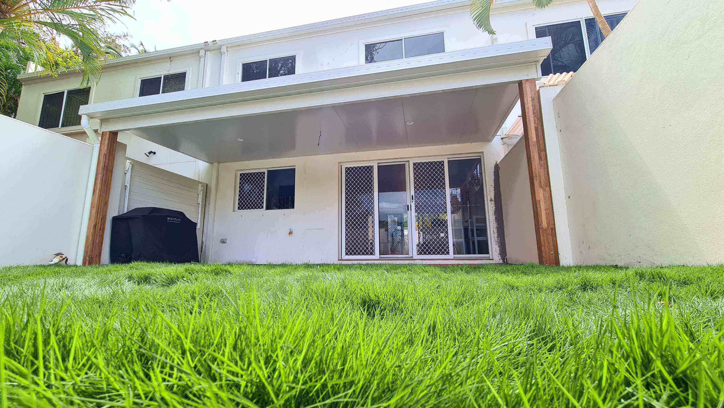 Modern insulated patio attached to a two-storey home, creating a shaded outdoor space with lush green lawn, ideal for backyard entertaining.