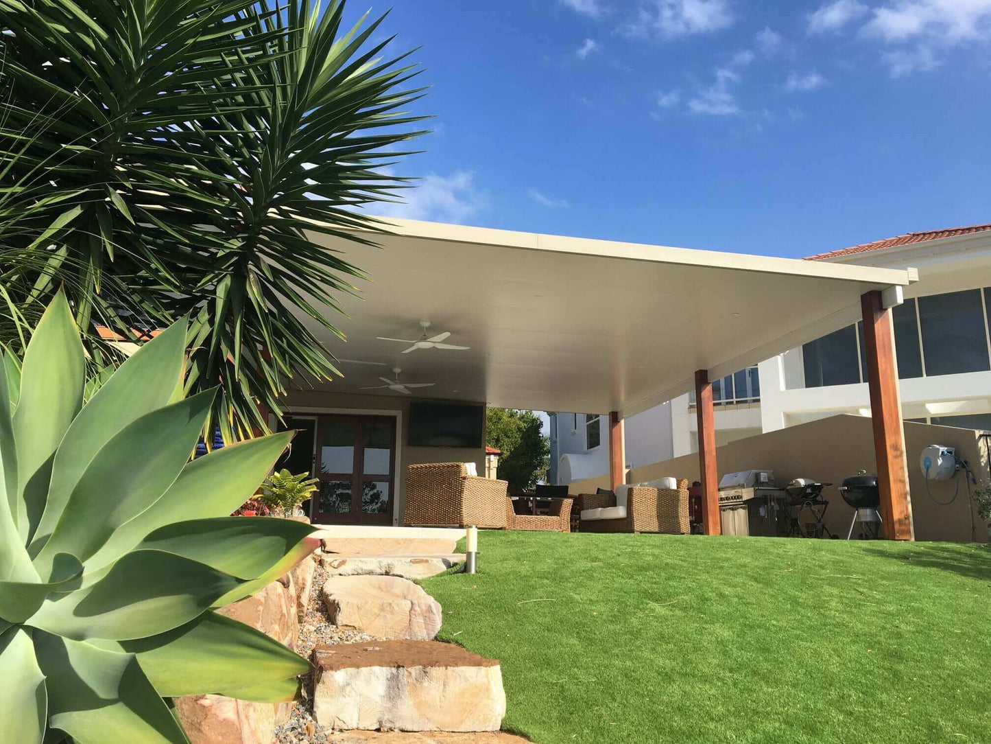 Spacious insulated patio with timber posts and ceiling fans, offering a stylish covered outdoor entertainment area overlooking a landscaped garden.