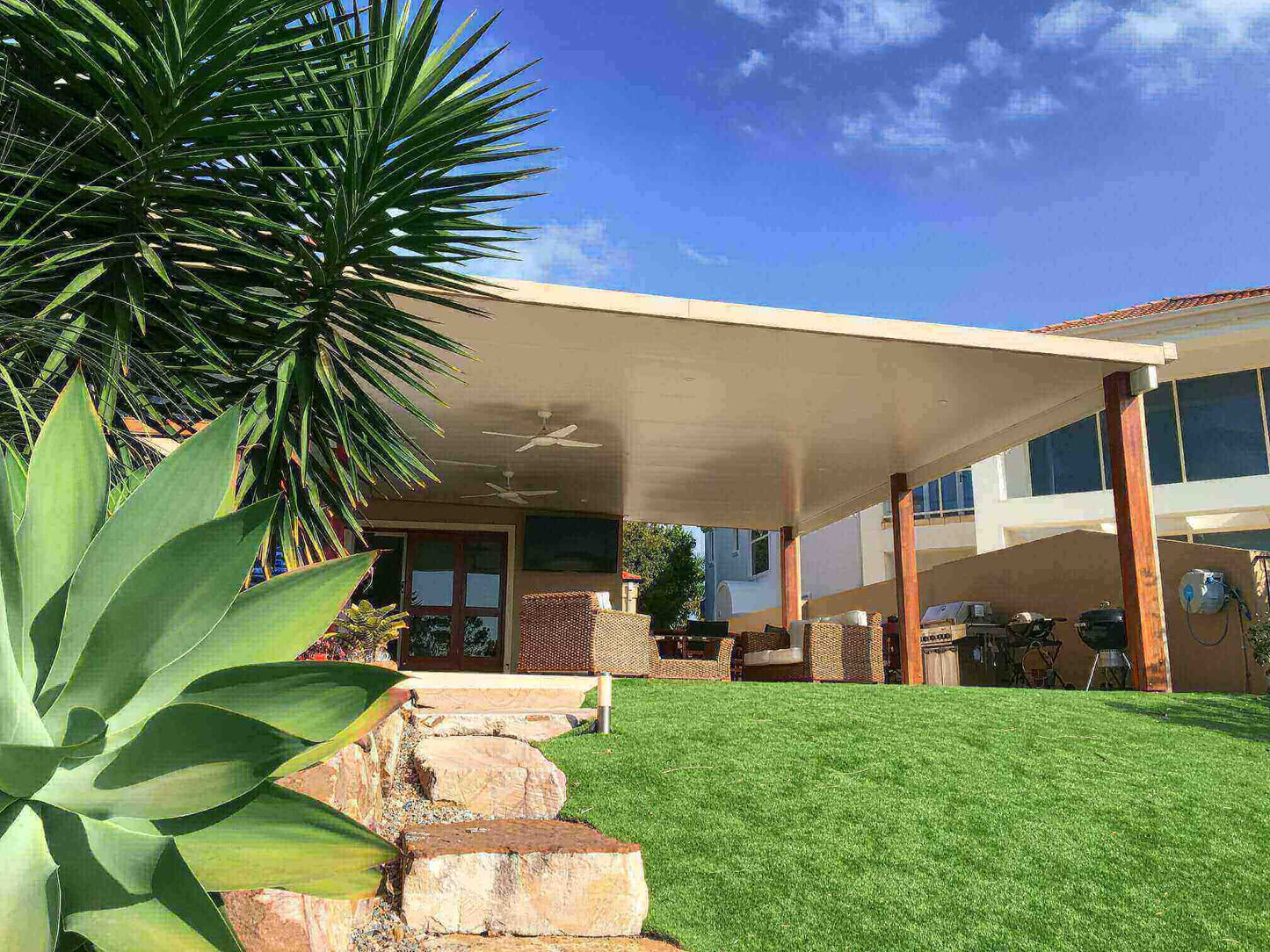 Insulated flat roof patio with timber posts and ceiling fans, creating a spacious covered outdoor entertaining area for an Australian home.