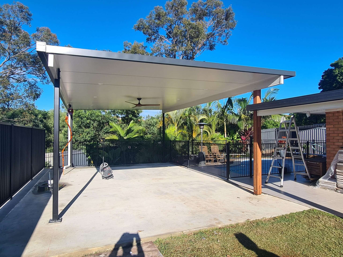 Insulated freestanding patio carport by the pool, combining timber and steel posts with ceiling fans, ideal for entertaining family and friends.