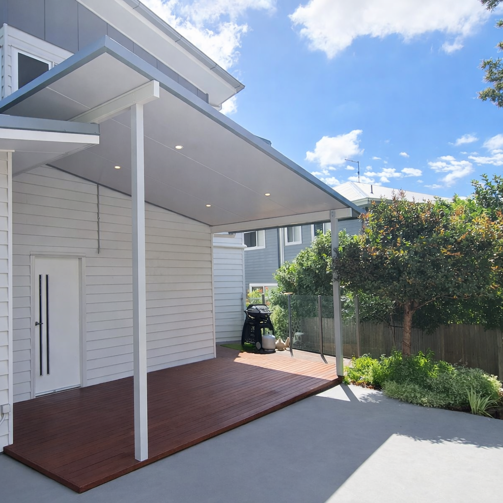 Skillion-style patio roof fixed to wall of a modern white two-storey home, featuring a clean flat underside with recessed downlights, slim white support posts, and grey fascia trim, extending over a timber deck area.