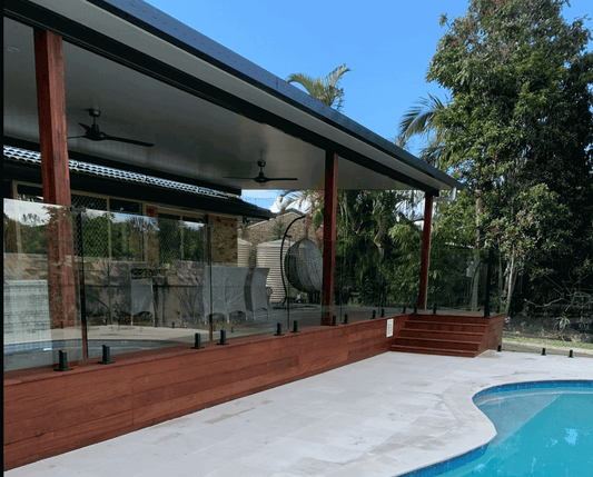 Contemporary insulated patio with wooden decking and glass railings, offering stunning pool views and surrounded by vibrant tropical plants for the perfect outdoor escape.