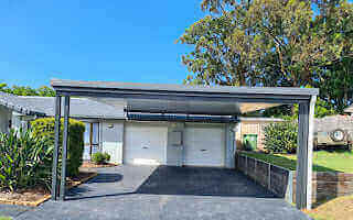 Basalt-finished insulated flyover patio carport, seamlessly coordinated with the home and retaining wall, featuring a trailer and convenient double garage access.