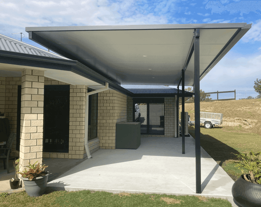 Modern insulated flyover patio and carport roof with a sleek concrete slab foundation, positioned beside a green storage shed for a balanced outdoor look.