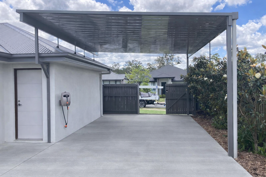 Flyover single-skin steel carport with a flat roof and slim support posts next to a residential property.