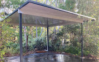 Free standing single skin patio carport with sleek steel frame surrounded by lush green trees and natural bushland.