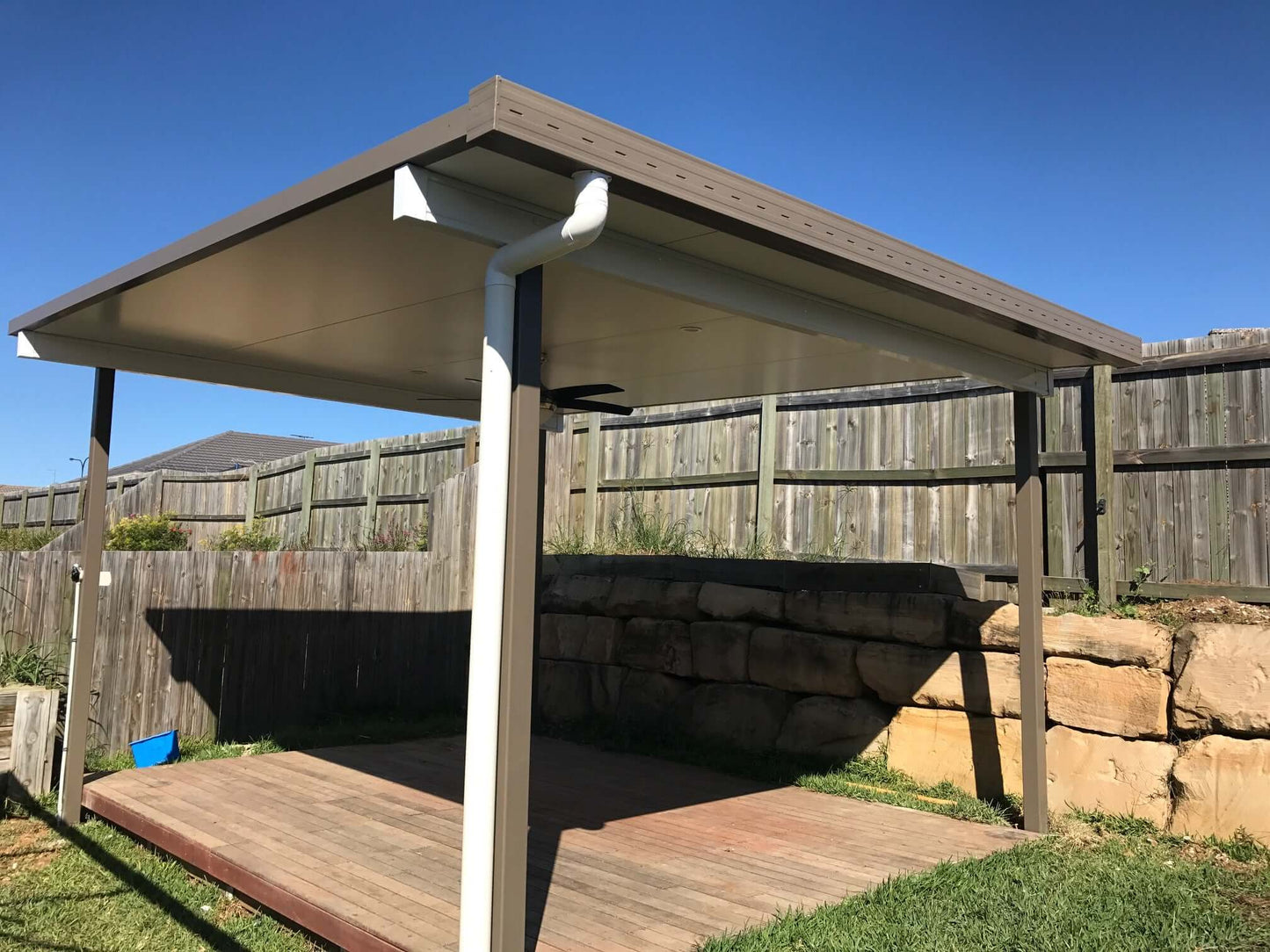 Single skin free standing patio installed at the rear of a yard near a retaining wall under clear blue skies.