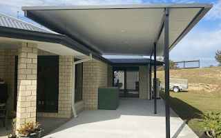 Insulated flyover patio roof in backyard of spacious home with high steel posts matching house color, creating cozy family-friendly outdoor space.