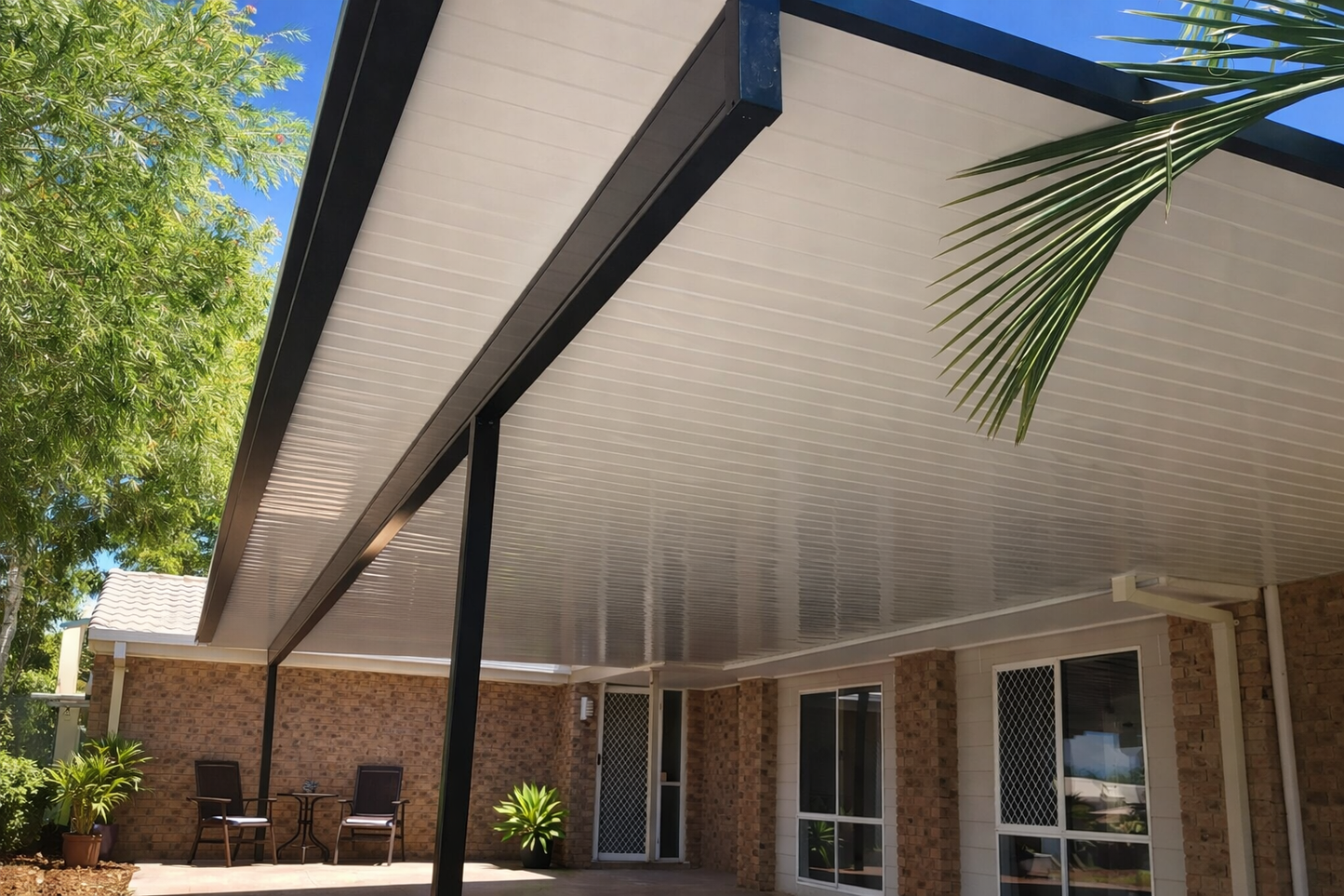 Modern insulated patio roof with white corrugated ceiling panels and black steel support beams attached to a brick home