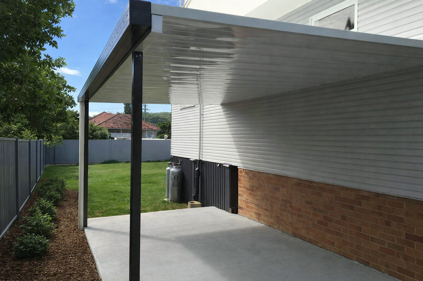 Modern flat, single-skin patio roof fixed to wall, featuring a sleek metal panel with a smooth, reflective finish, supported by slim black steel posts; creating a clean, minimalist outdoor covered area. 