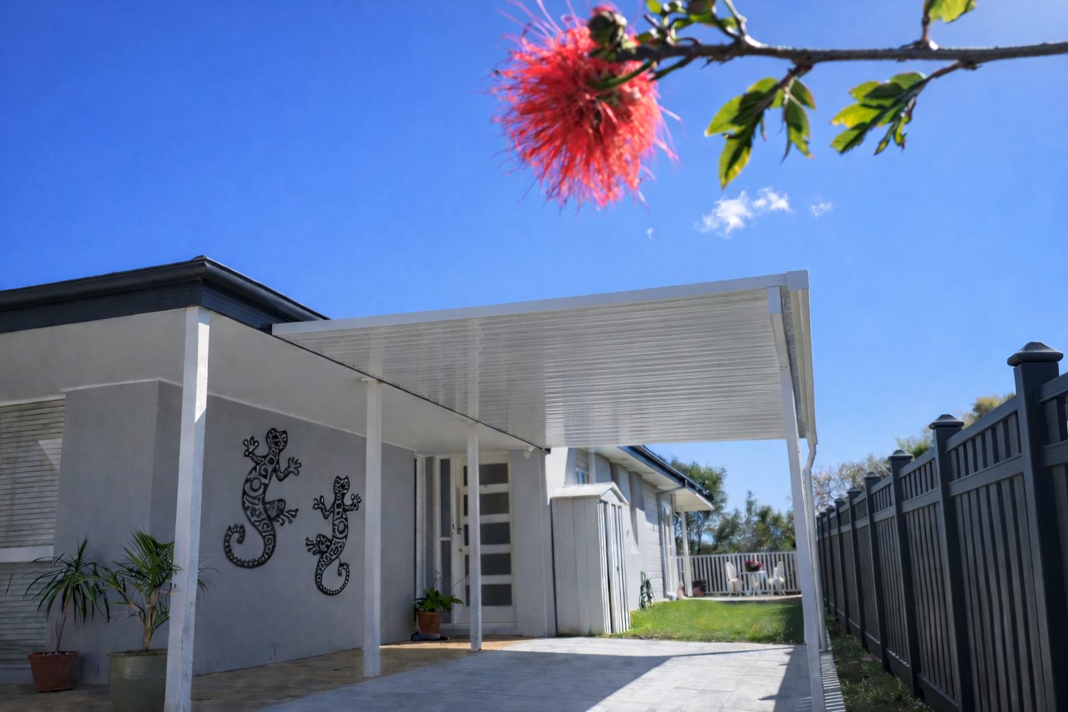 White corrugated patio roof fixed to fascia, extending over a paved outdoor area and supported by slim white posts.