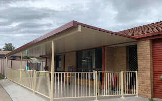 Attached single skin patio extension with a sloped roof and safety railing, creating a sheltered outdoor area alongside a brick home.
