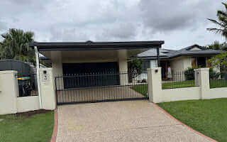 Functional and elegant flyover carport roof, attached to brick columns in a secure gated section, coordinated with the house and garage roof, with a gentle drop to the driveway.