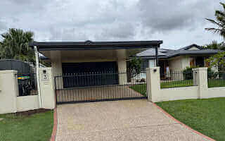Sleek modern single skin carport with a flat roof seamlessly extending over the driveway, offering stylish cover to a double garage in a contemporary home setting.