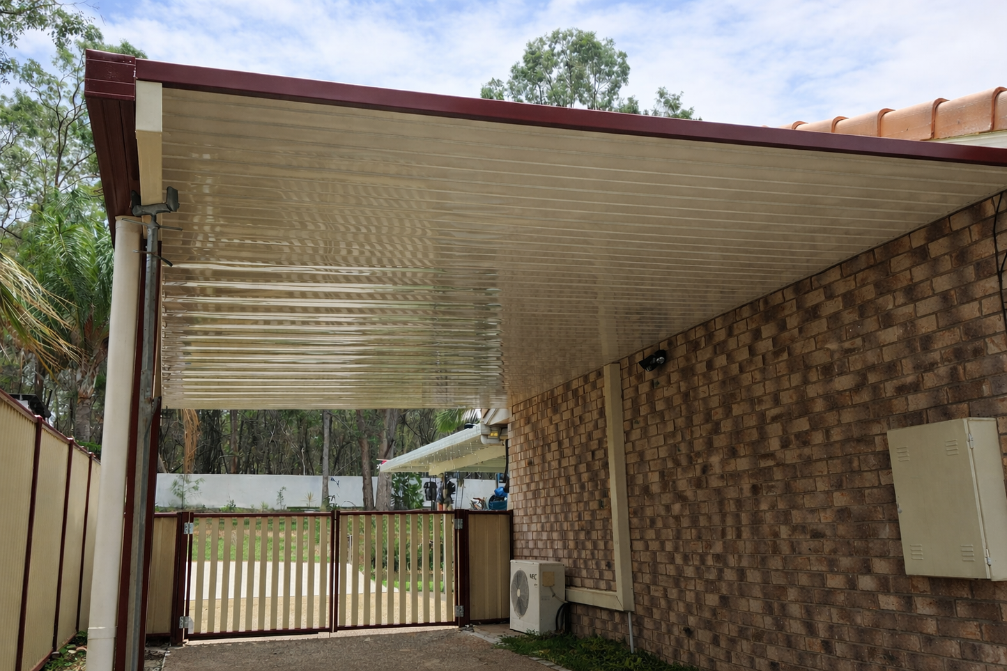 Covered side patio with cream corrugated metal roof and red trim attached to brick house