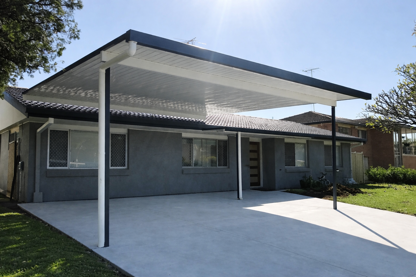 Modern single-skin flyover carport with a flat white roof and contrasting dark frame, installed over a concrete driveway