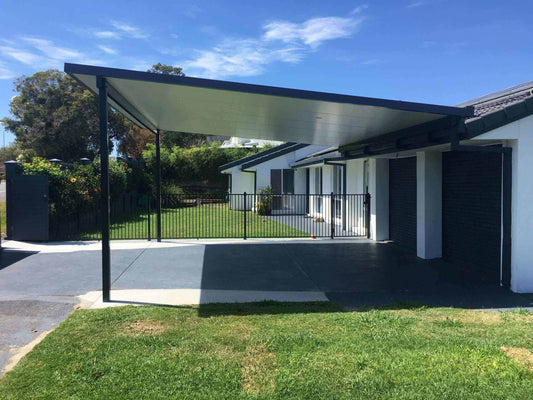 Contemporary insulated reverse fall carport with sleek steel posts attached to a modern home, offering weather-protected parking beside a front yard.