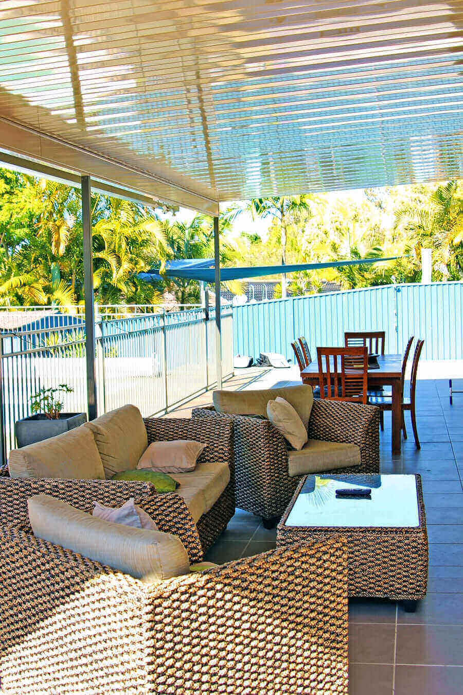 Single-skin patio roof with sleek steel posts providing a shaded outdoor dining area beside a pool, surrounded by tropical garden views.